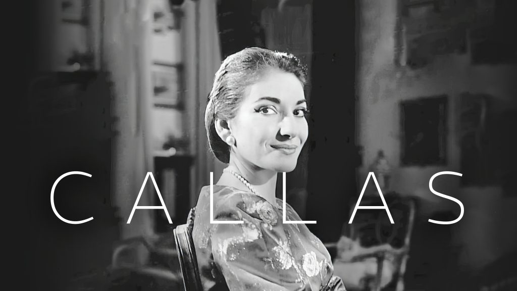 Maria Callas sits in a chair looking at the camera, the word Callas is set over the image. 